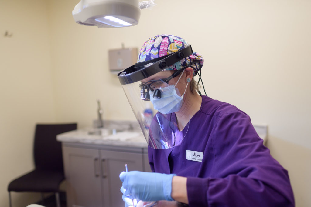 Registered Dental Hygienist with faceshield performing a dental checkup